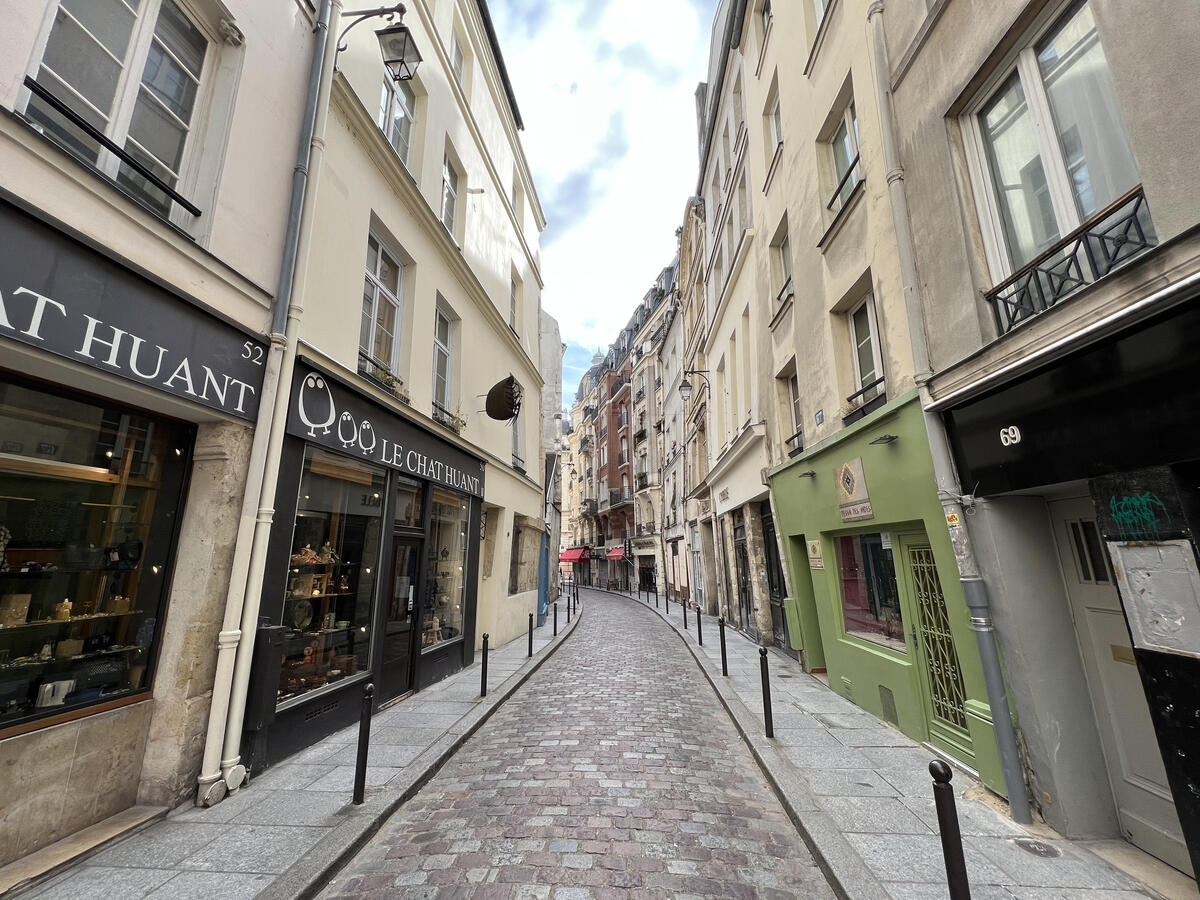 Narrow cobblestone street lined with small boutiques and pastel buildings in a historic Paris neighborhood.