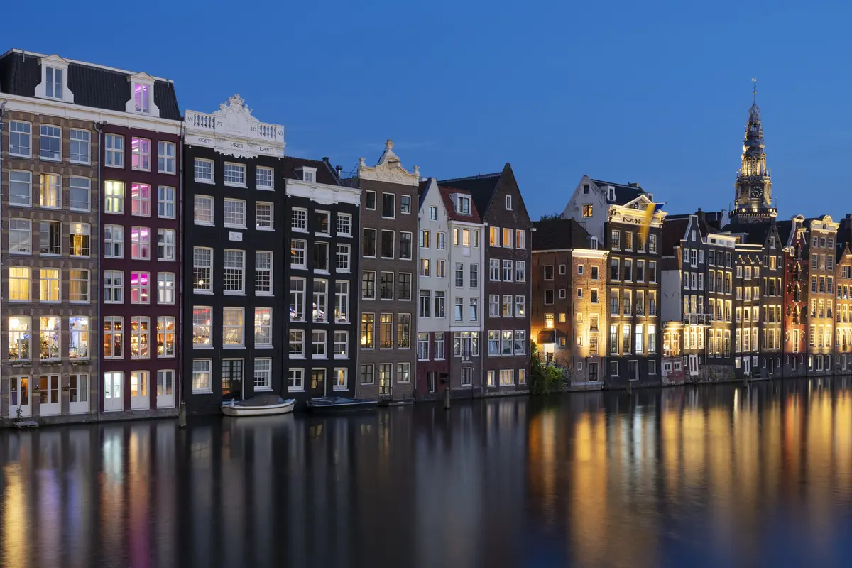 Row of illuminated canal houses reflected in the water at dusk.