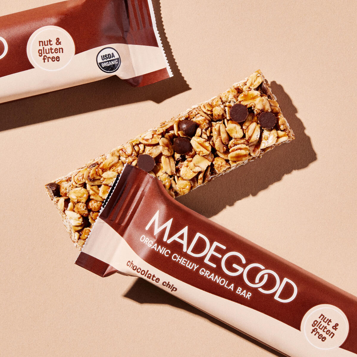 An unpackaged MadeGood® Chocolate Chip Chewy Granola Bar sits under a packaged granola bar