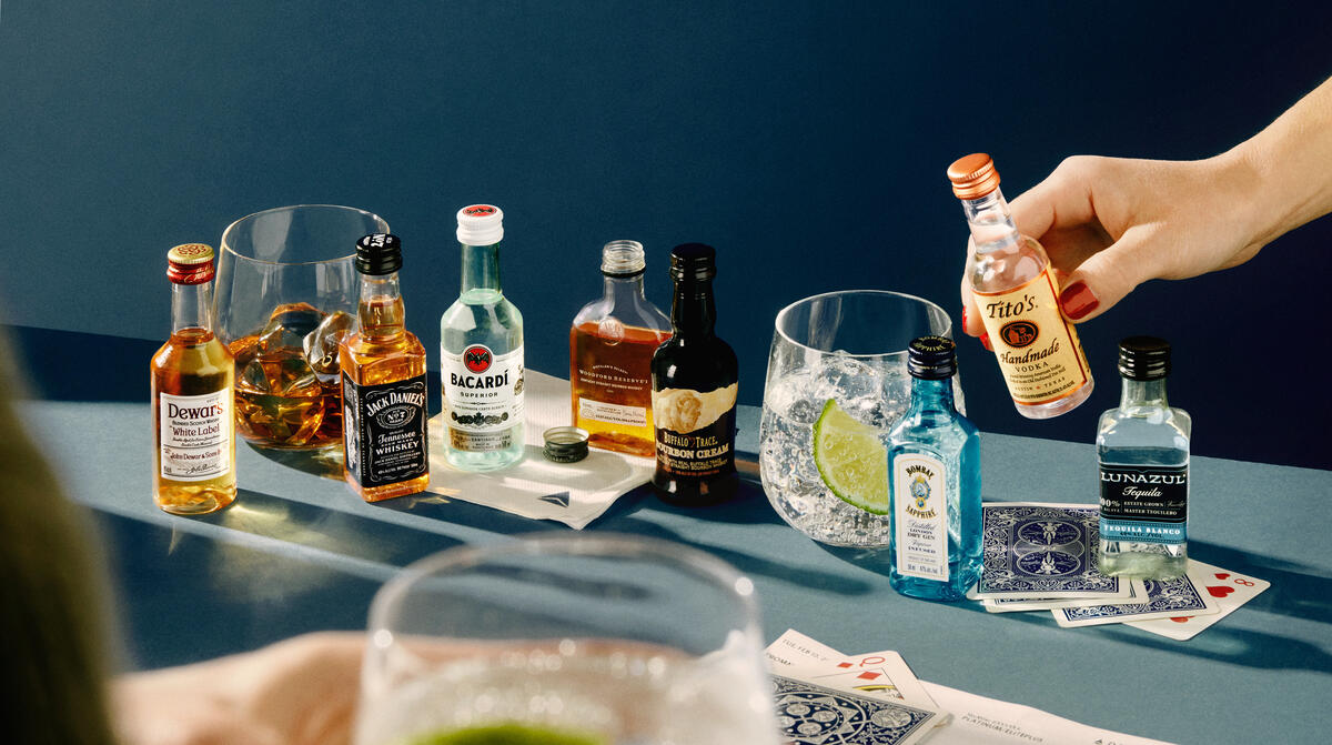 A lineup of airplane bottles of alcohol against a blue background