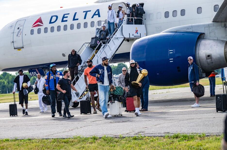 People exit a Delta airplane via stairs on the tarmac, with one person carrying a gold trophy while others hold bags nearby.