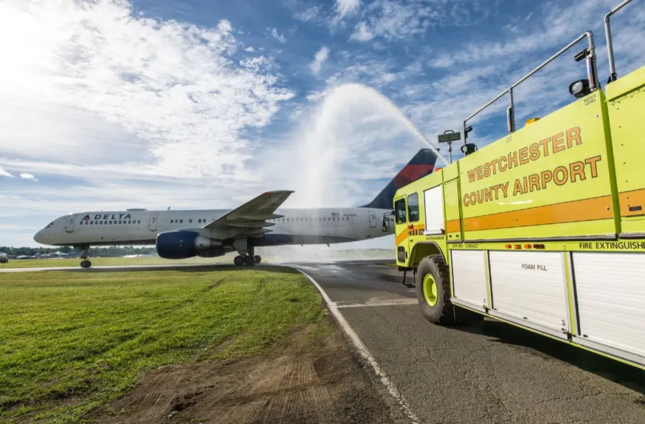 Delta airplane receives water salute from airport fire truck on runway.