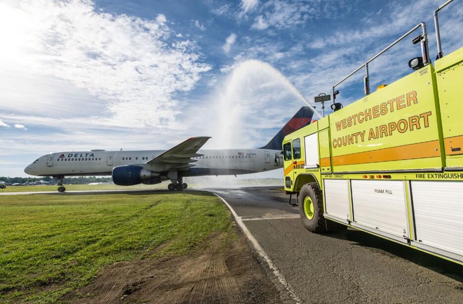 Delta airplane receives water salute from airport fire truck on runway.