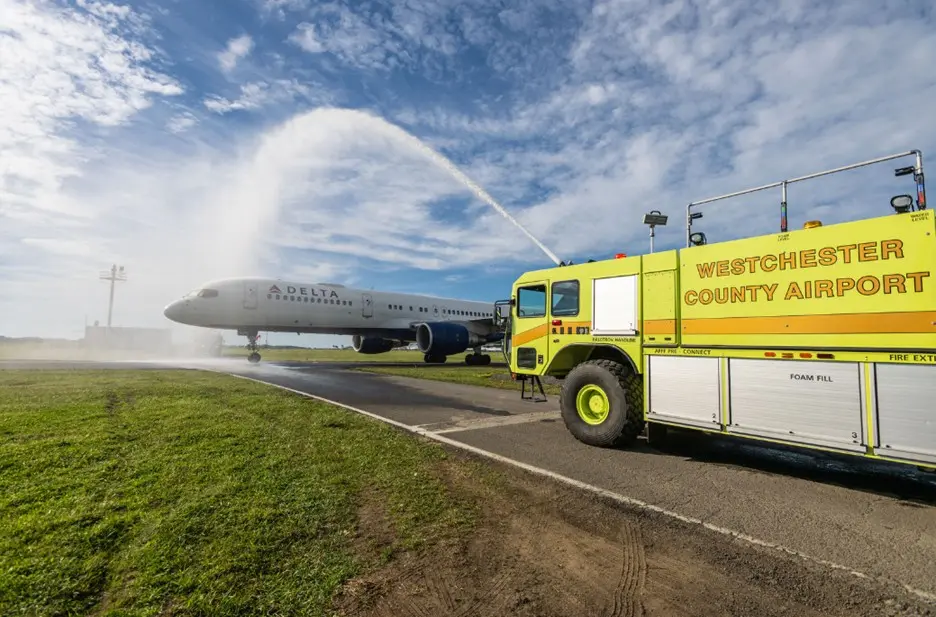 Delta airplane receives water salute from airport fire truck on runway.