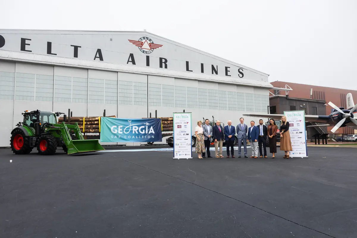 Group stands in front of Delta Air Lines’ historic hangar at the Delta Flight Museum alongside a tractor, timber load and Georgia SAF Coalition signage during a sustainable aviation fuel event.