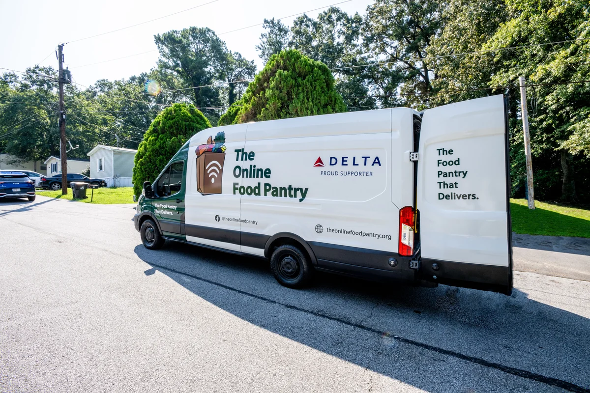 The Online Food Pantry delivery van, supported by Delta, parked in a neighborhood with its rear door open.