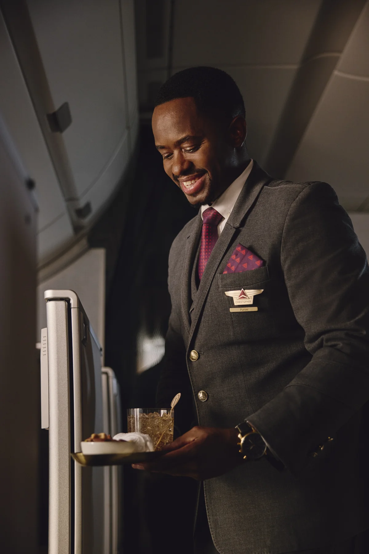 Flight attendant presents a welcome drink and snack service in the Delta One cabin.