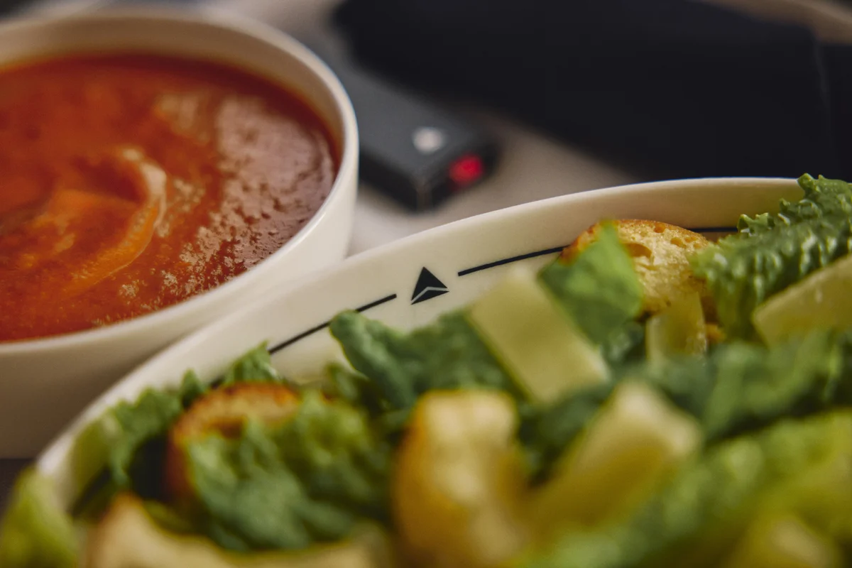 Bowl of tomato soup served alongside a fresh green salad with croutons on an airline meal tray.