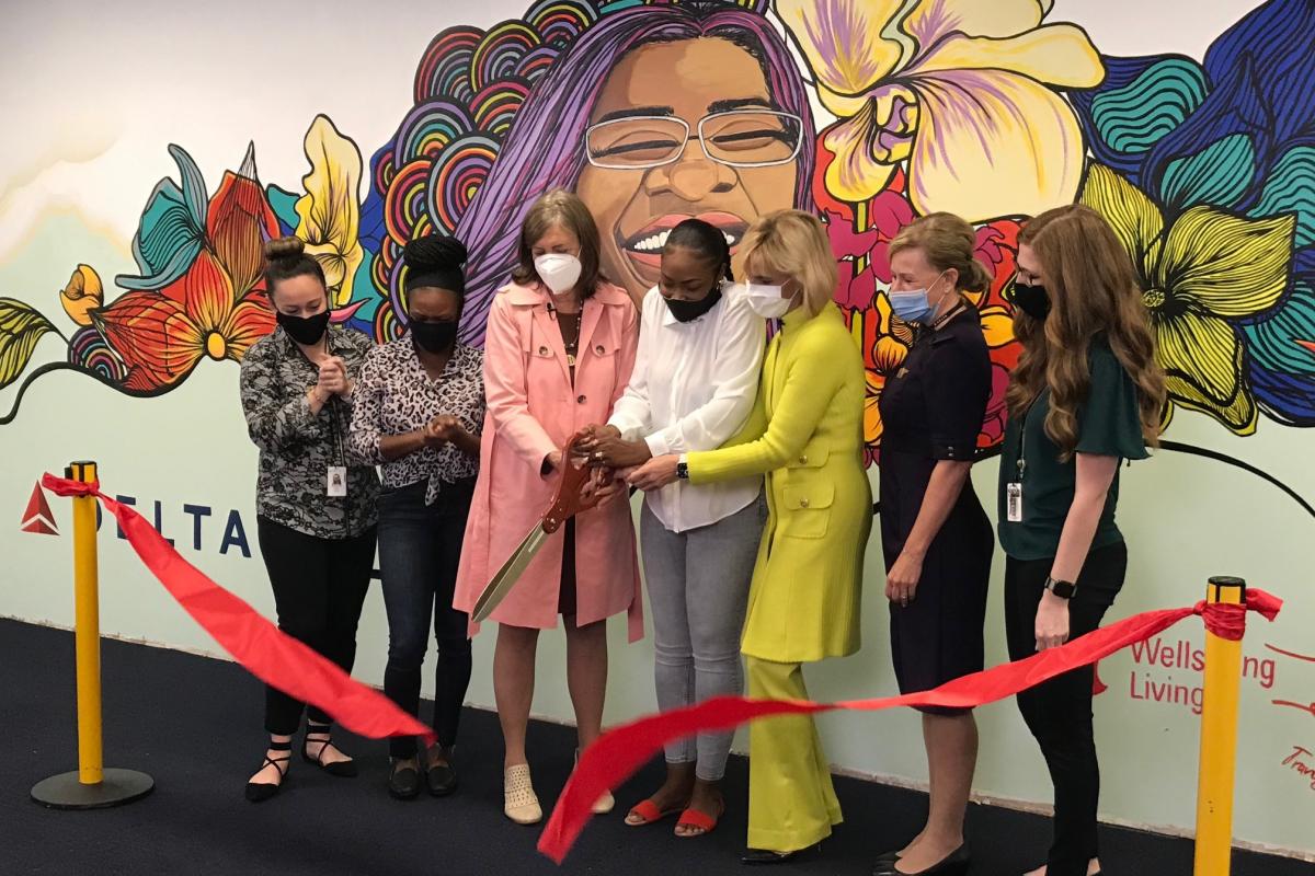 Wellspring and Delta leaders and employees cut a ribbon to present the final mural that symbolizes Delta's mission to combat human trafficking. The mural is of a smiling woman with flowers and rainbows behind her head. Beneath the image is the word 'free' and an imagery for Delta and Wellspring's partnership.