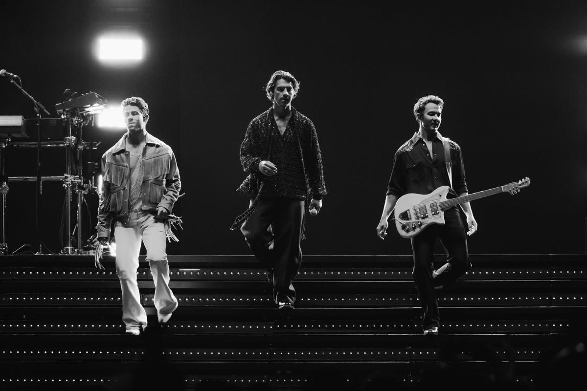 The Jonas Brothers walking on stage stairs during concert in black and white.