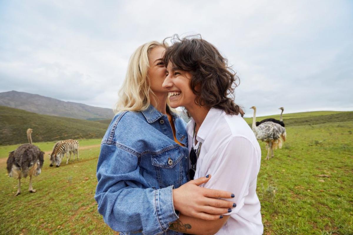 Two women smiling with ostriches and zebras behind them