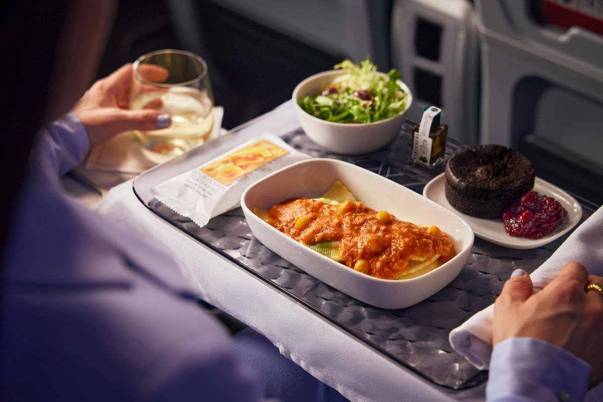 A meal served on Delta Premium Select: Spinach and Ricotta Tortellini, tossed in red pepper mascarpone sauce, accompanied by roasted vegetables, crumbled feta, and nut-free basil pesto, with a decadent dessert: Chocolate Brownie Passion Fruit Bar  