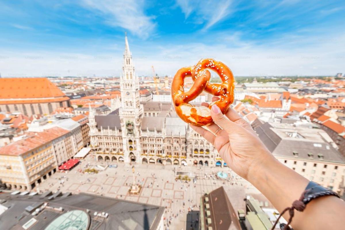 A tourist's hand holds a German pretzel against the backdrop of the city of Munich.