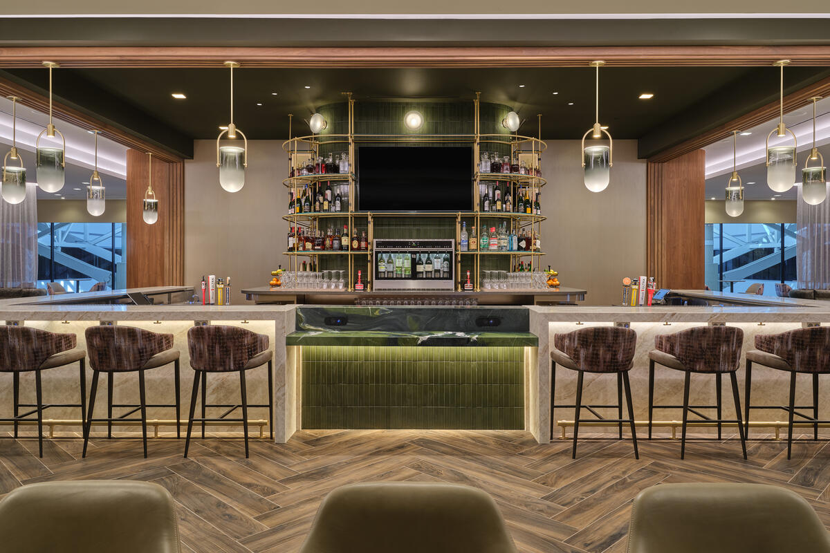 Front view of lounge bar with high‑back stools, illuminated shelving, pendant lights and wood‑pattern flooring