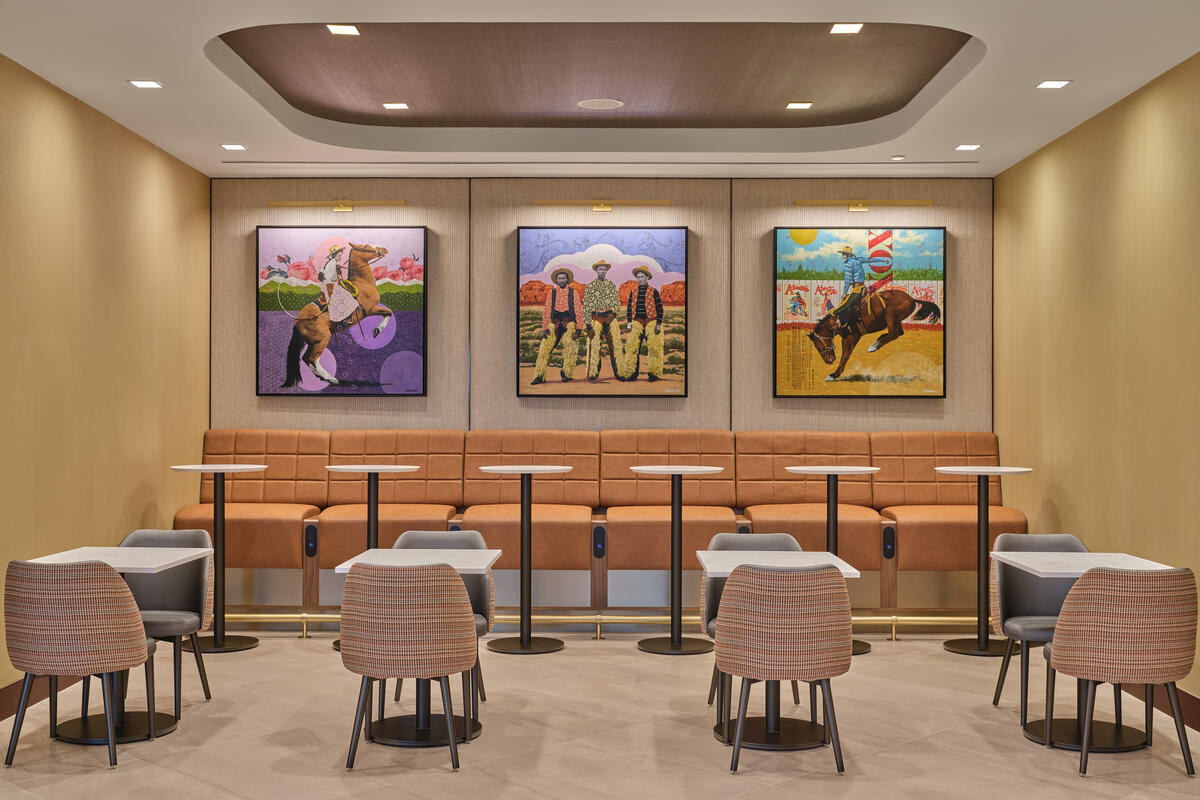 Seating nook with woven chairs, high-back bench seating, small tables and three colorful art pieces displayed on the wall