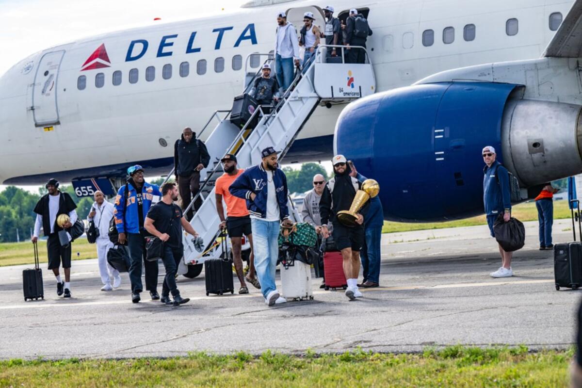 People exit a Delta airplane via stairs on the tarmac, with one person carrying a gold trophy while others hold bags nearby.