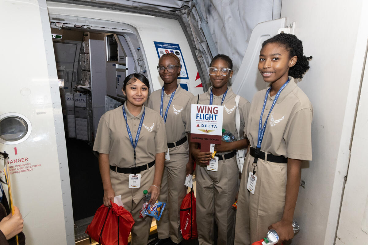 Students pose at an aircraft doorway during the WING Flight experience, holding event materials and giveaway bags.