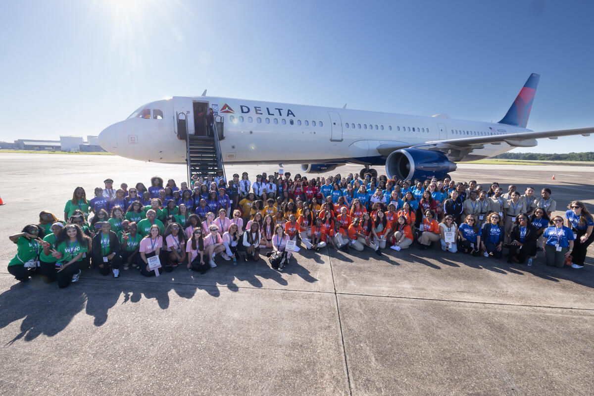Large group of WING Flight participants gathered on the tarmac in front of a Delta aircraft during Girls in Aviation Day.