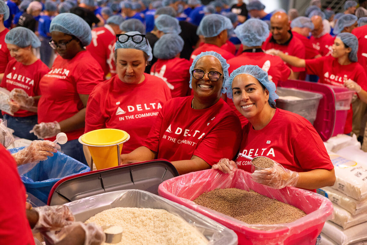 Voluntários da Delta, vestindo camisetas vermelhas, luvas e toucas de cabelo, recolhem os ingredientes e os montam.