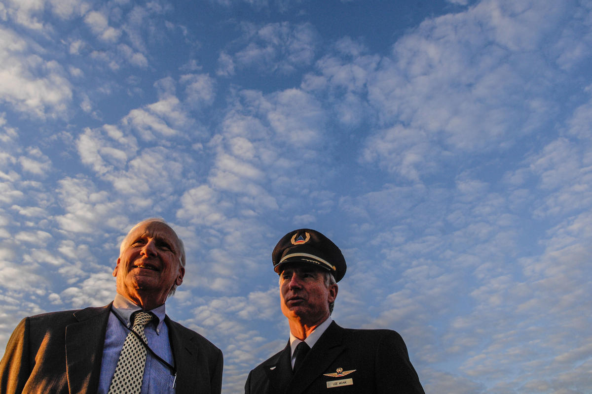 Former Delta CEO Jerry Grinstein stands with a Delta pilot against a blue, cloudy sky.