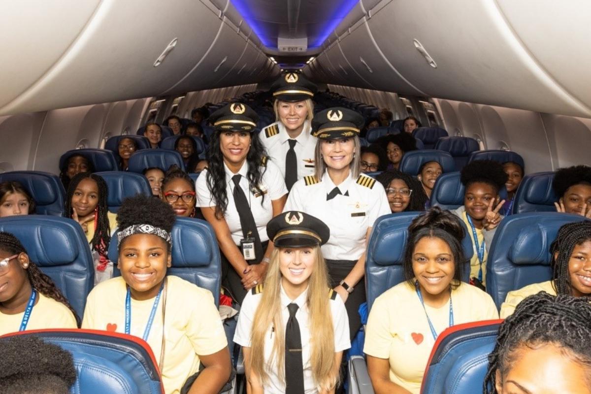 The girls selected for Delta's WING Flight 2023 pose with Delta pilots on the plane.