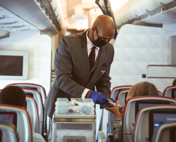 A masked flight attendant serves customers.