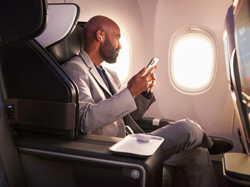 A Delta customer sits in Delta's First Class cabin, holding their phone.